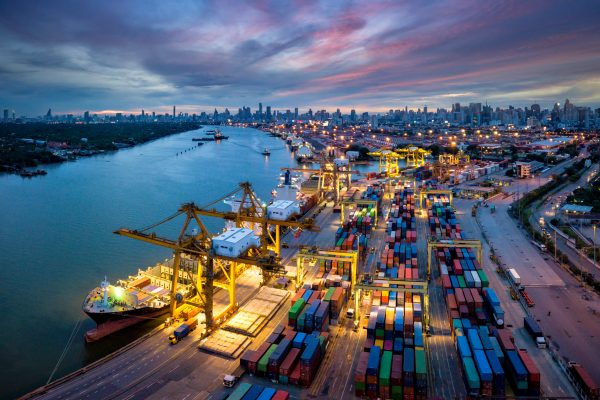 Aerial view of international port with Crane loading containers in import export business logistics with cityscape of Bangkok city Thailand at night